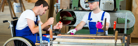 Ein Mann mit Behinderung zieht in einer Schreinerei die Schraubzwingen am Holz fest