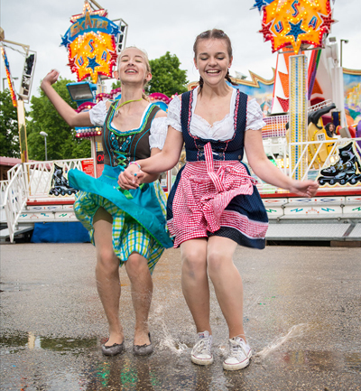 Zwei junge Frauen tanzen in Tracht auf der Dult in Regenpfützen 