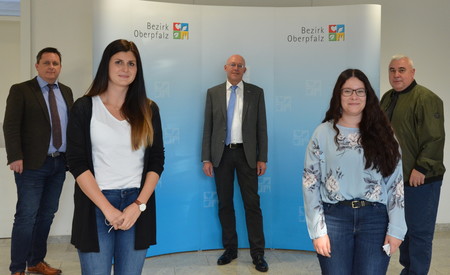 Fünf Menschen stehen vor Fotowand und lächeln.