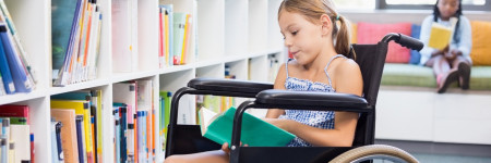 Ein Mädchen sitzt lesend im Rollstuhl vor einer Regalwand mit Büchern