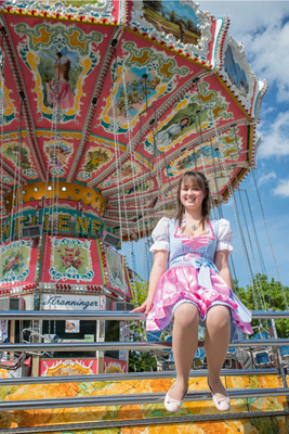 Eine junge Frau in Tracht sitzt vor einem Kettenkarussell