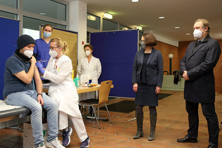 Vier Personen beobachten die erste Impfung gegen das Corona-Virus am medbo-Bezirksklinikum Regensburg.