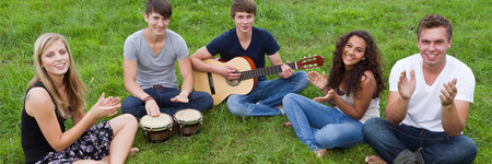 Jugendliche auf der Wiese klatschen zum Rhythmus der Gitarre und der Bongos