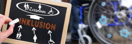 Auf einer Schiefertafel ist die Bedeutung von Inklusion geschrieben und gezeichnet: Das "Zusammen"-sein von Menschen mit und ohne Behinderung, im Hintergrund die Räder eines Rollstuhls